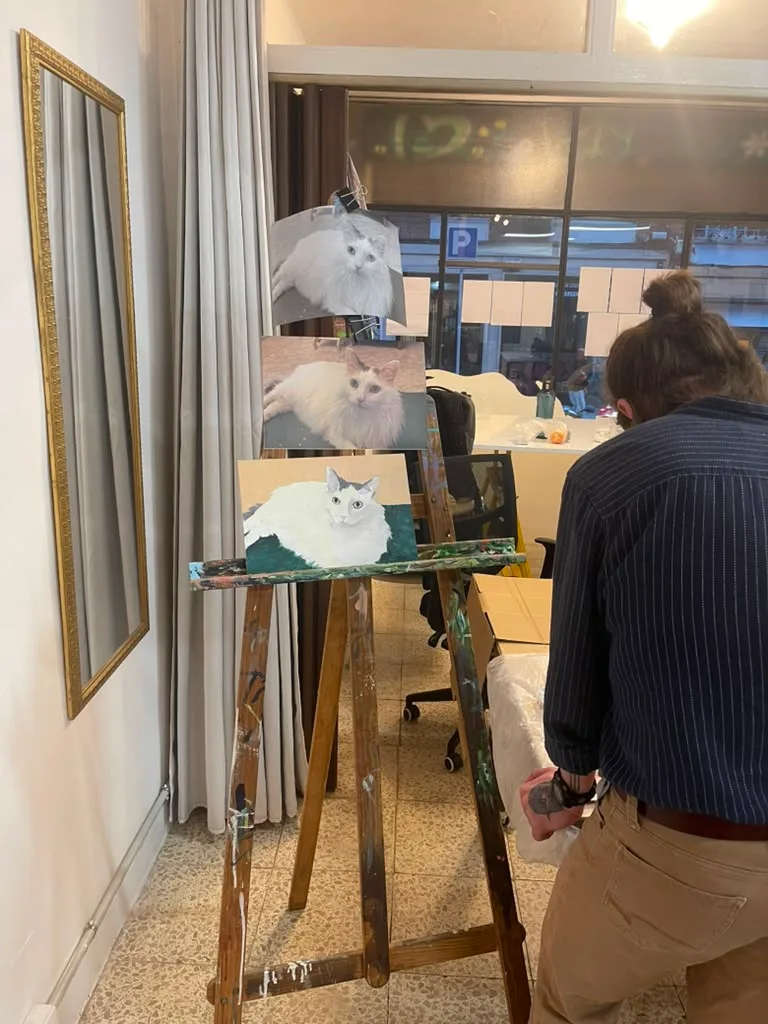 Three stages of the white cat on one easel while a painter works nearby.