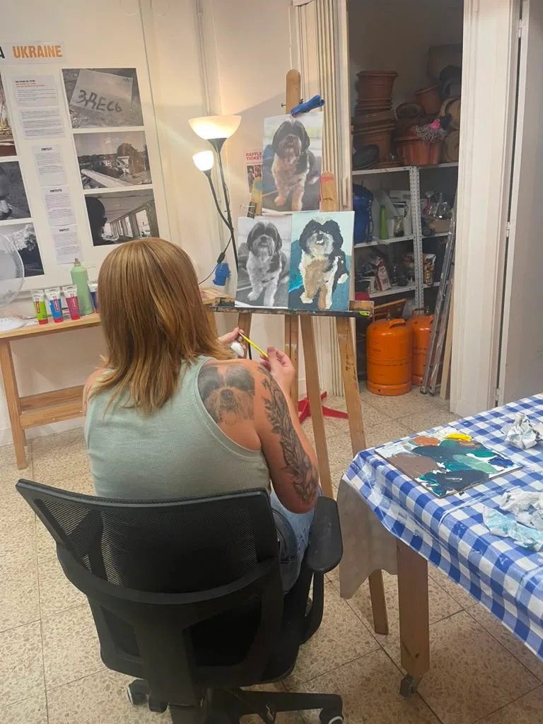 A painter seen from behind, working on the shih tzu with the reference above.