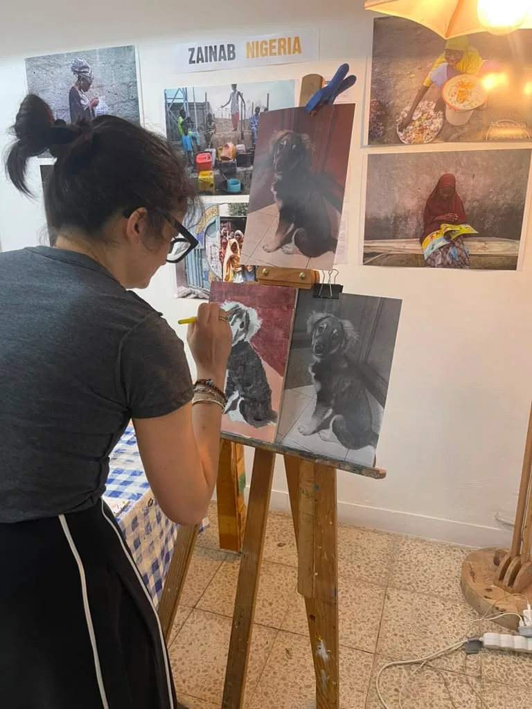 A painter working on the puppy portrait, with the reference above the easel.