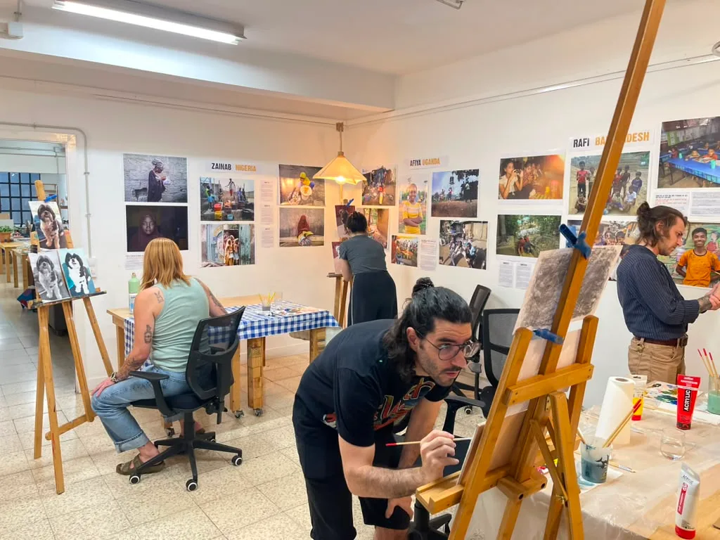 Four painters at their easels in the studio, with photographs on the walls.