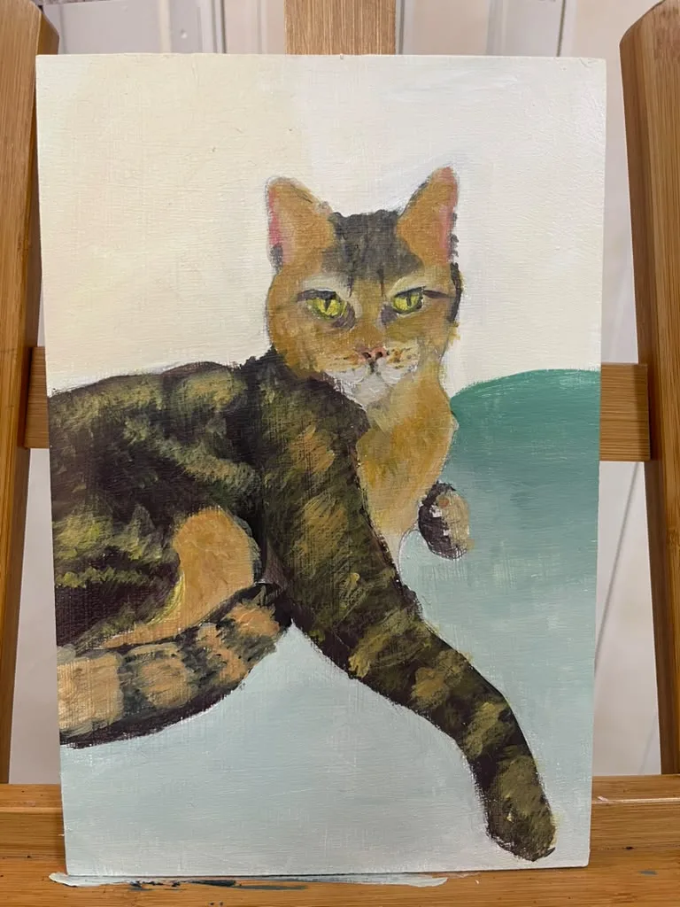 A finished oil painting of a tabby cat lying on a teal blanket, on the easel.